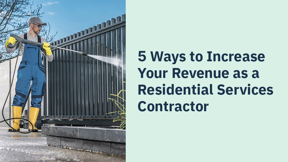 Contractor in protective gear pressure washing a dark metal fence outdoors